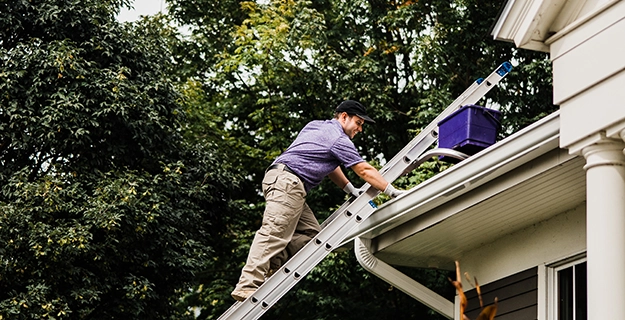 Window Genie service professional climbing on a ladder to clean the gutters of a home.