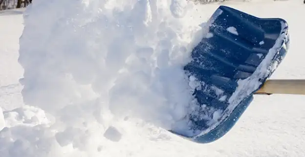 Snow flying from a blue shovel.