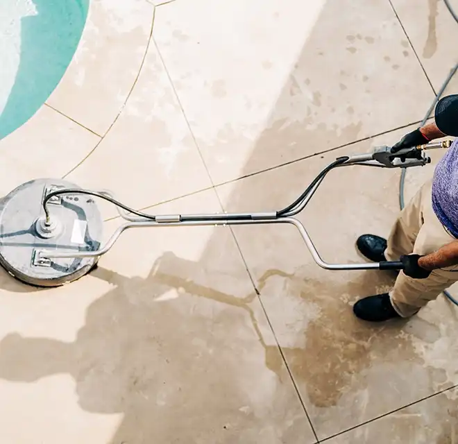 Window Genie service professional using a professional-grade pressure washer to clean a stone patio.