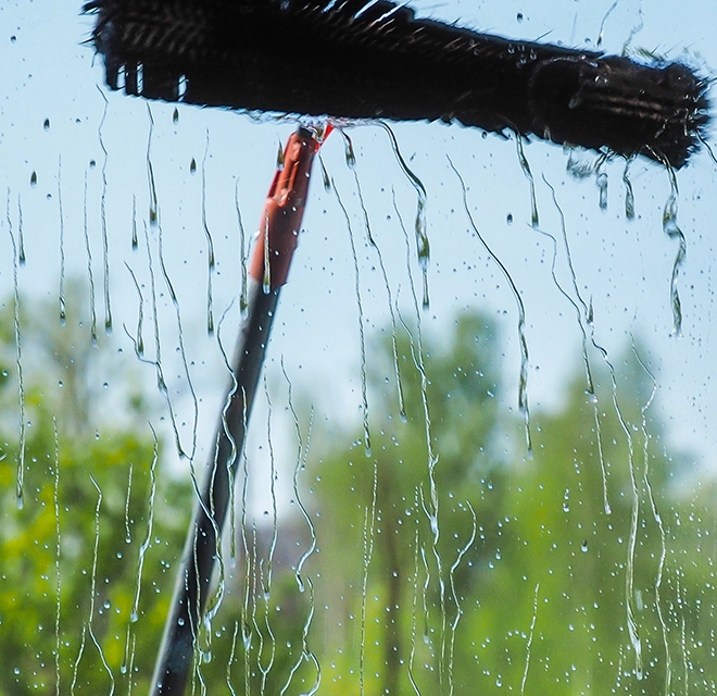 A large scrub brush being used to wash a window.