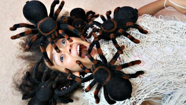 A girl lying on the ground with three fake spiders on her and her mouth open in a scream.