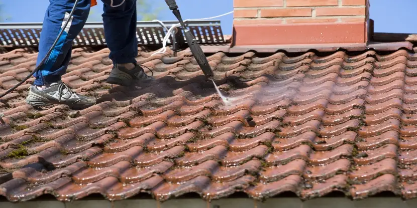 Person pressure washing the roof with a high-pressure water washer machine.
