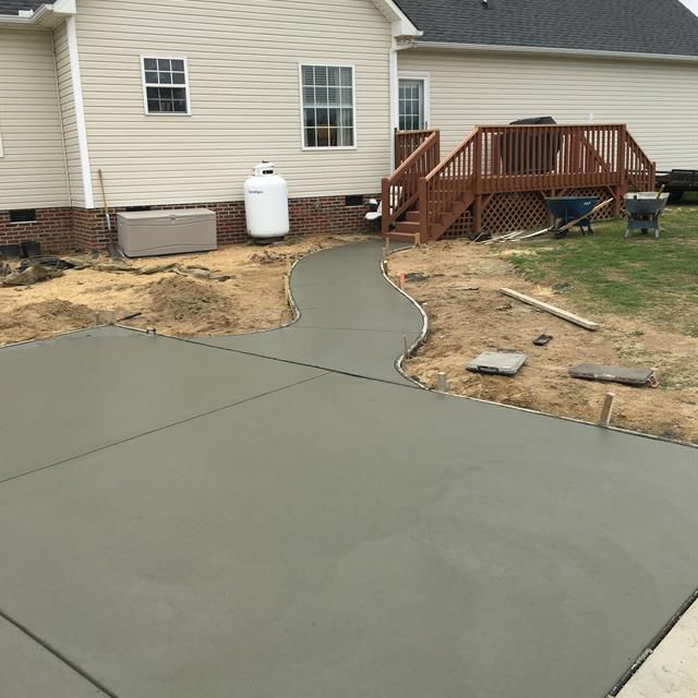 A pathway in construction on the house's backside with a deck in the background.