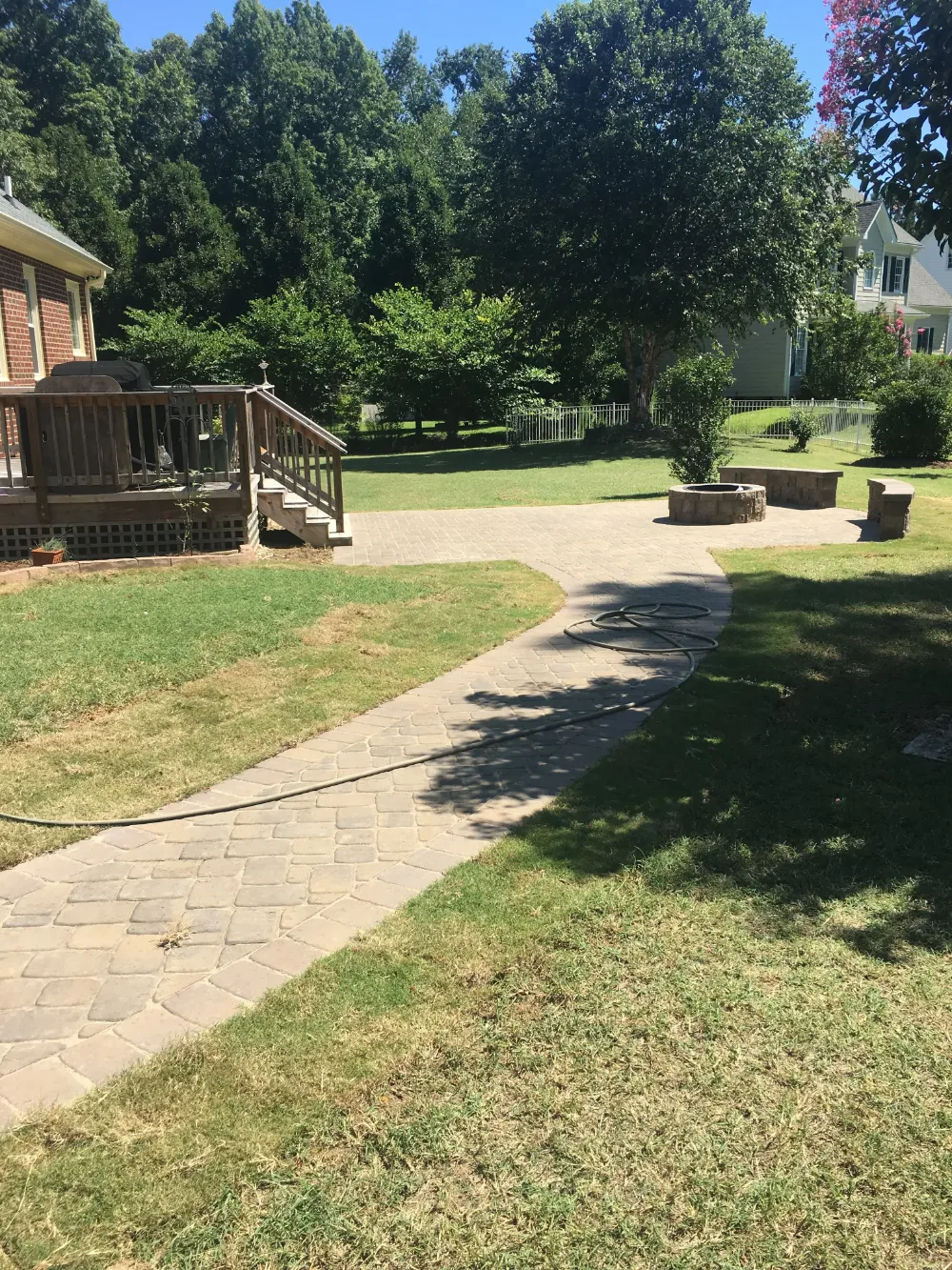 Hose on brick pathway shaded by tree