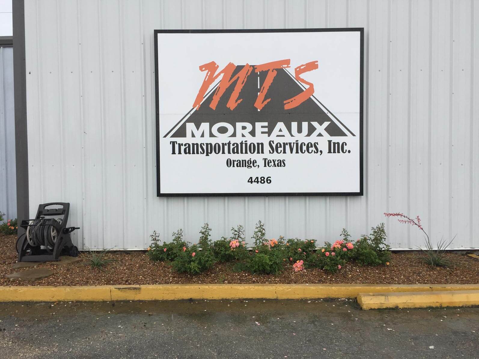 MTS sign on white fence above flower landscaping
