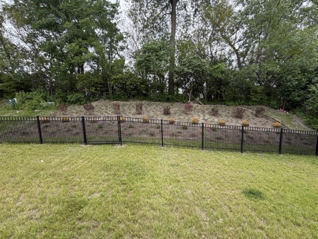 New hillside landscape installation in McHenry, IL featuring fresh shrubs and mulch behind a black aluminum fence surrounded by mature trees.