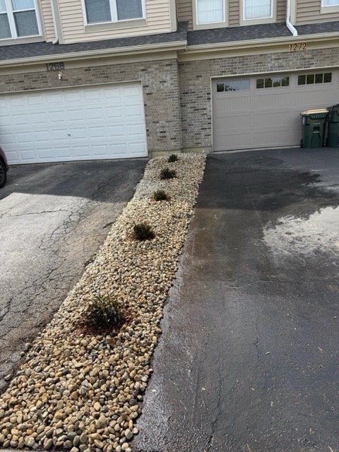 Decorative rock bed landscape renovation in Mundelein, IL with low-maintenance shrubs installed between two residential driveways.