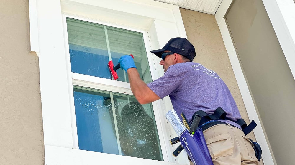 A Window Genie technician using a razor blade to clean the window of a new construction home.