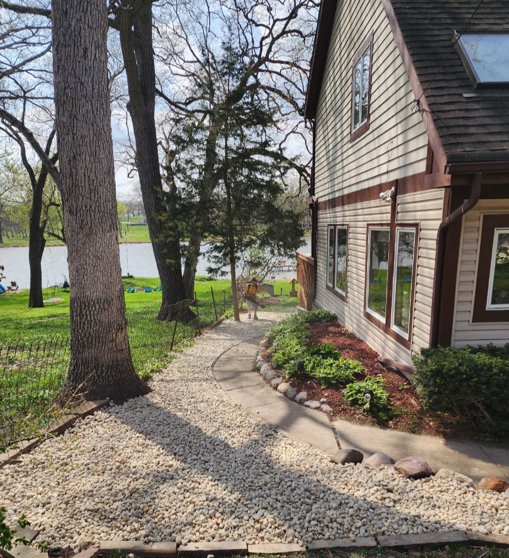 Newly installed river rock pathway alongside a lakefront home, bordered with natural stone and mulch beds, completed by a professional landscaping company serving Libertyville and surrounding areas