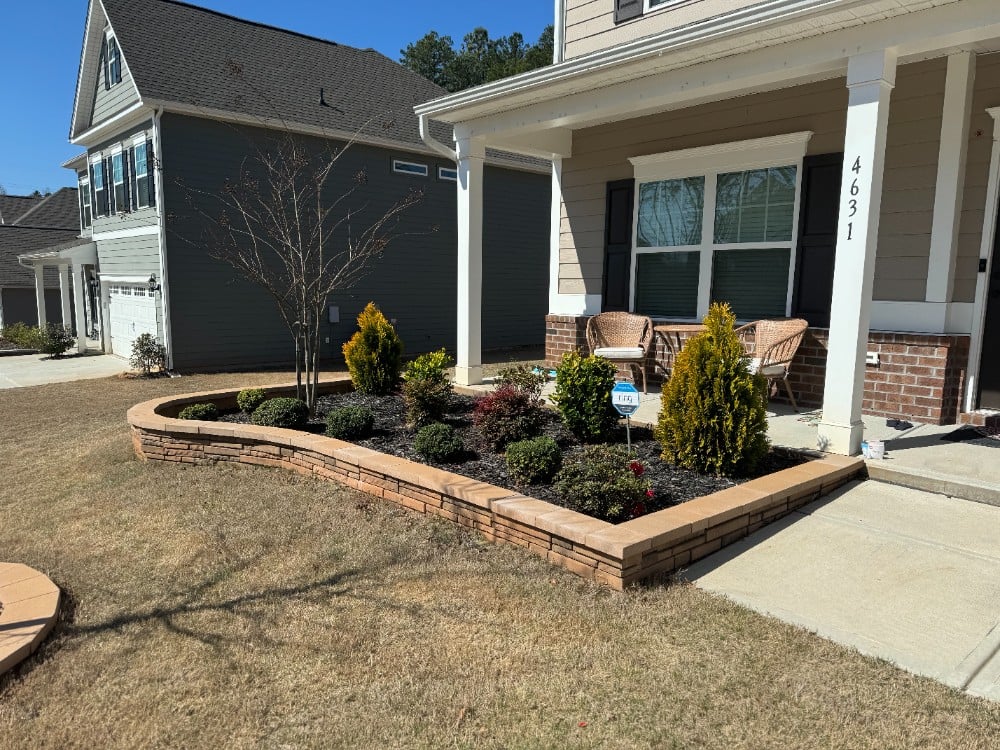 Brown stone raised landscape wall border for front yard bed. Included fresh mulch and curated bushes/trees/plants to complete the look!
