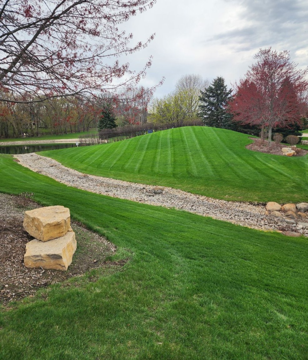 Professionally striped lawn with drainage swale, maintained landscape beds, and trimmed grass in McHenry, IL by a local landscaping company