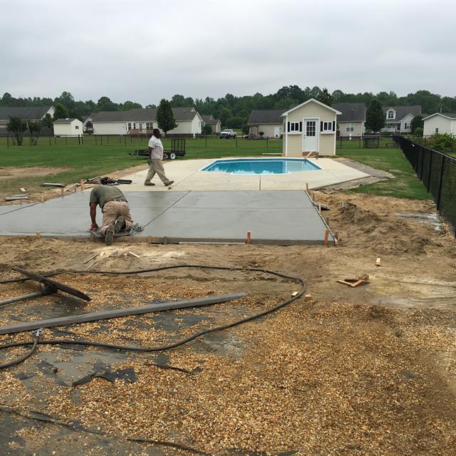 Two guys working on a pathway with a swimming pool and houses in the background.