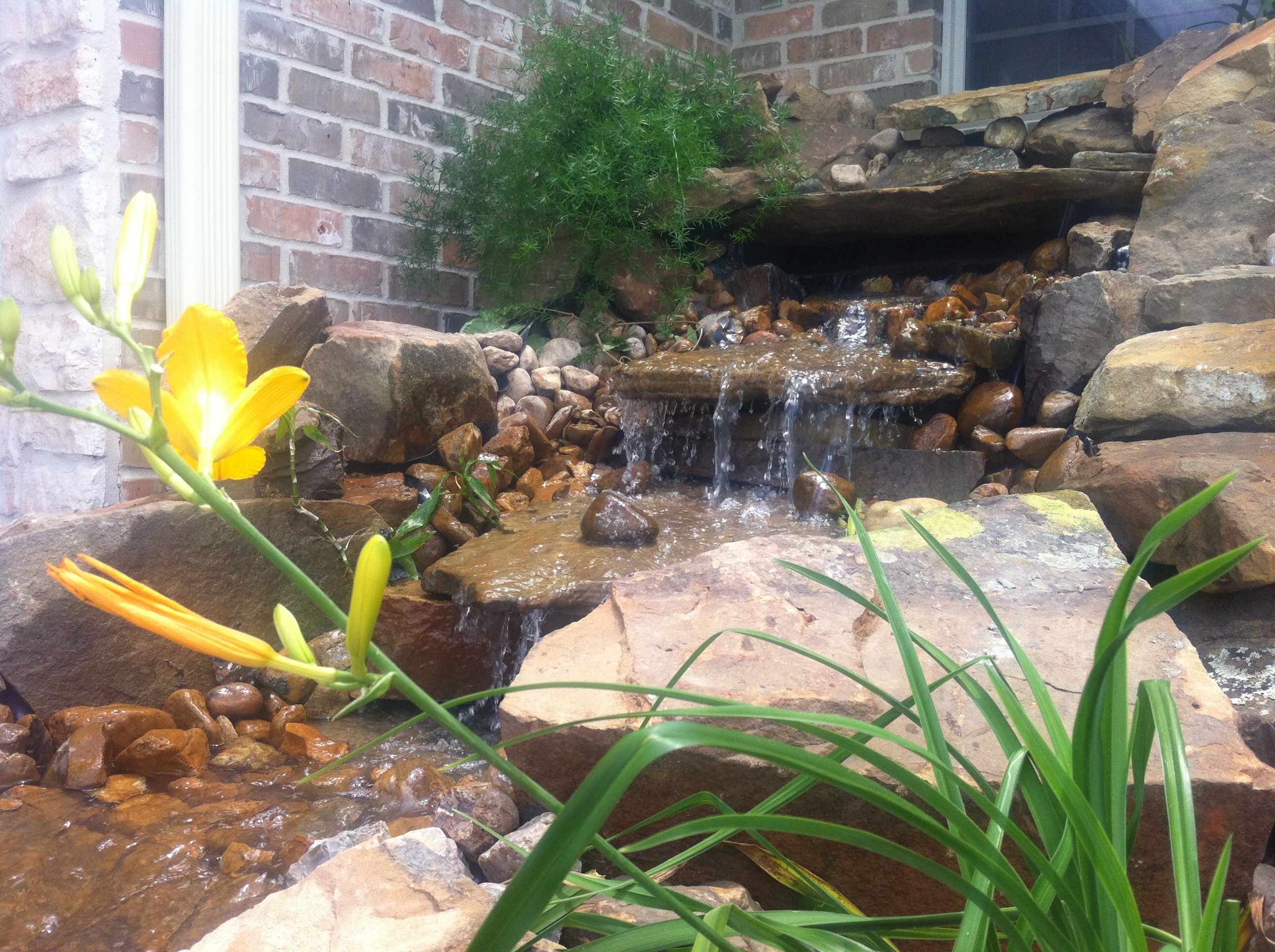 rock waterfall fixture cascading from brick house 