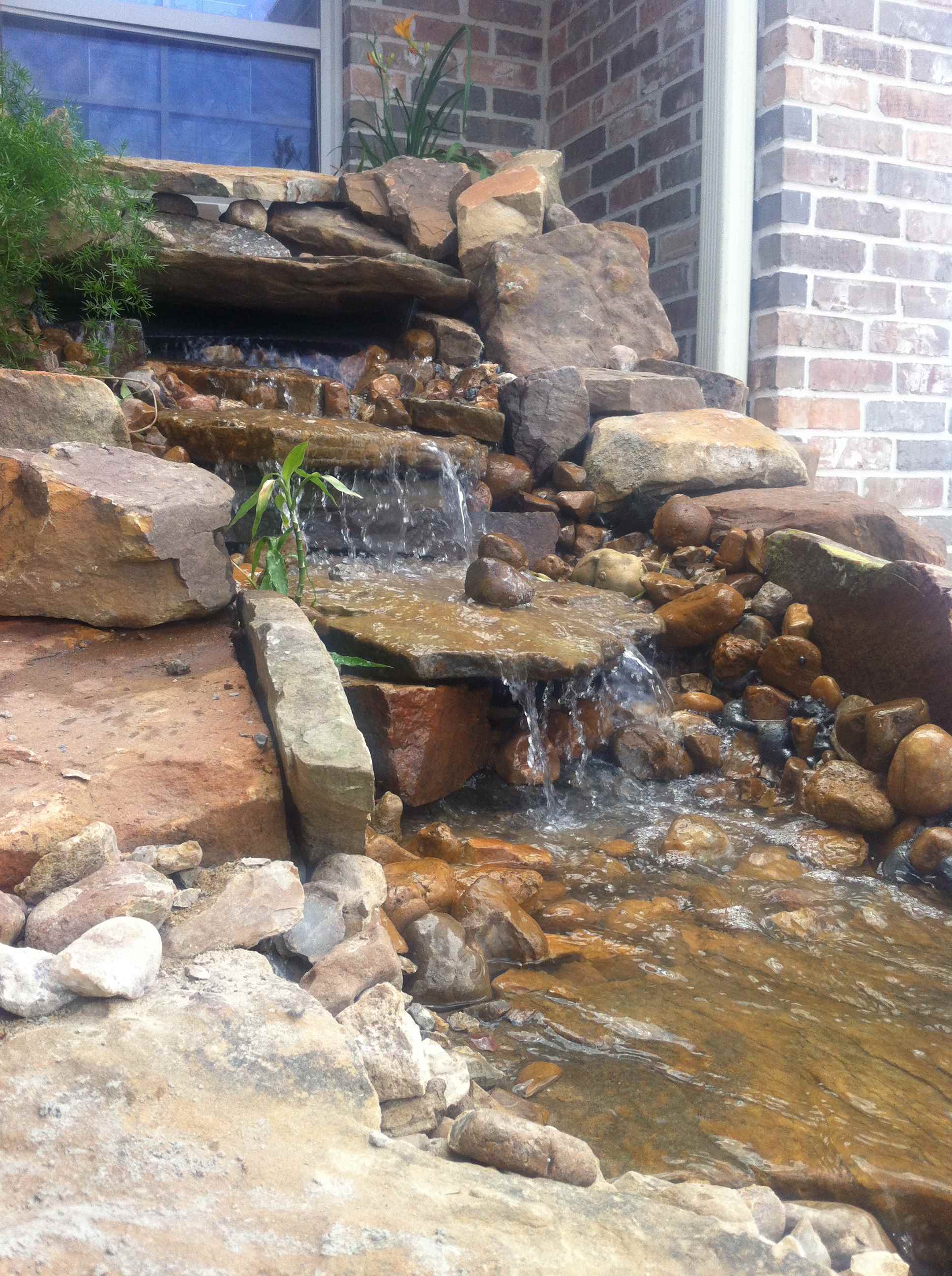 rock waterfall fixture cascading from brick house 