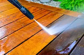 Pressure washer with black nozzle being used to clean wood deck.
