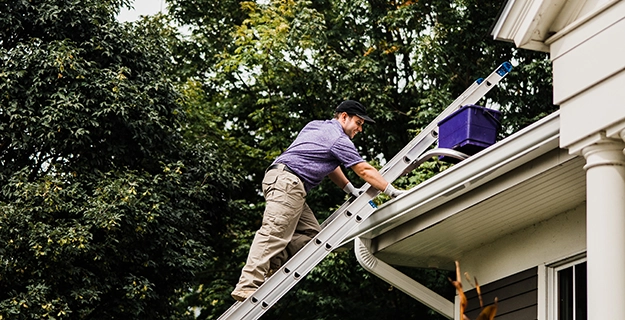 Smiling Window Genie service professional on a ladder cleaning the gutters of a home.