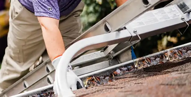 Window Genie service professional climbing on a ladder to clean the gutters of a home.