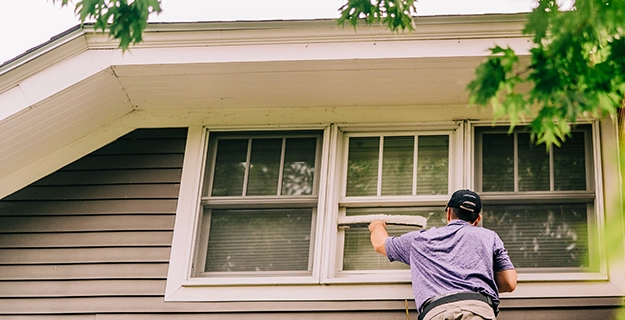 Window Genie service professional on a ladder cleaning the exterior of a home's second-floor windows.