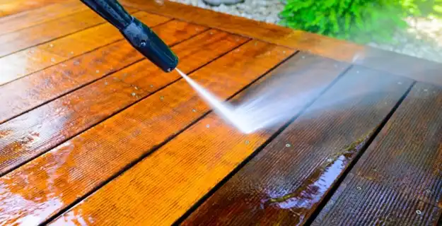 A pressure washer being used to clean a wood deck.