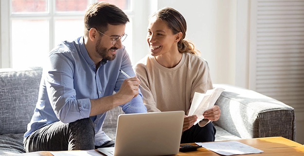 Couple reviewing papers and laptop in their living room.