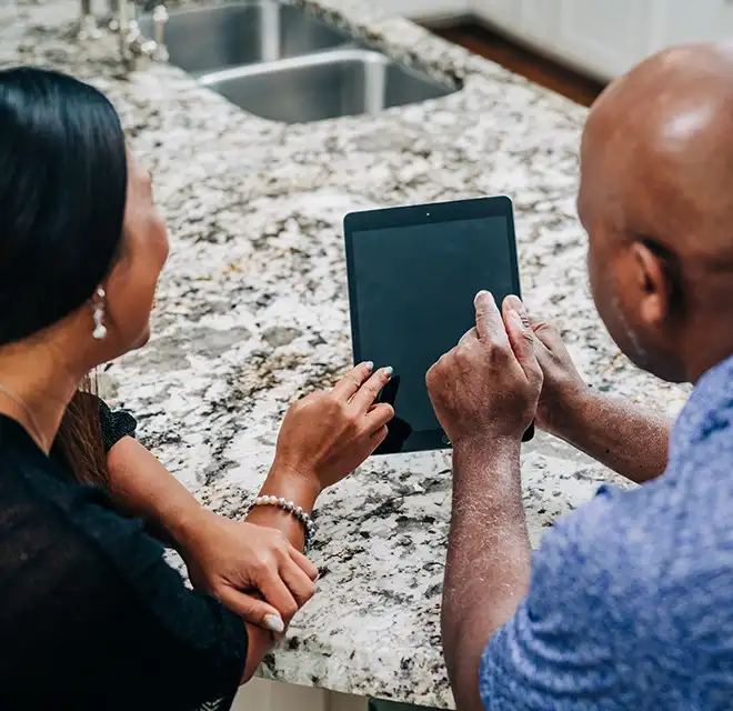 Customer sitting with Window Genie service professional at kitchen island reviewing tablet.