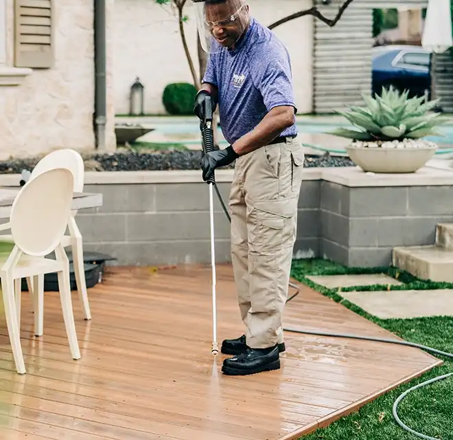 Window Genie technician pressure washing a deck in a backyard.