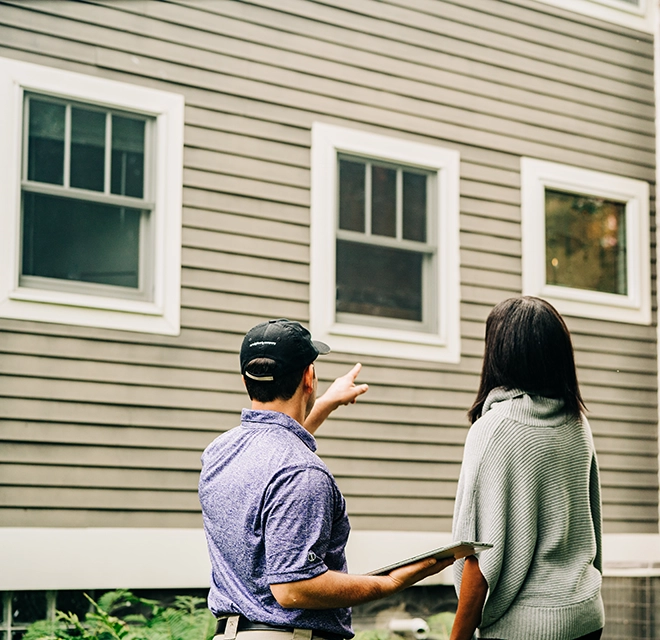 A Window Genie service professional standing next to a customer outside her home and pointing to windows.