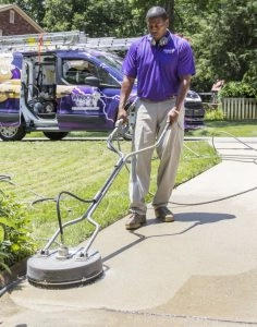 A window genie staff operating a lawn mower while pressure washing.