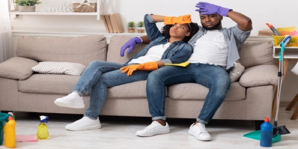 A couple sitting on a couch surrounded by cleaning supplies.