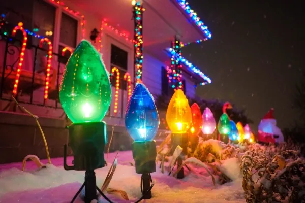 Close-up of colored holiday lights in the front yard of a residential home with snow on the ground.