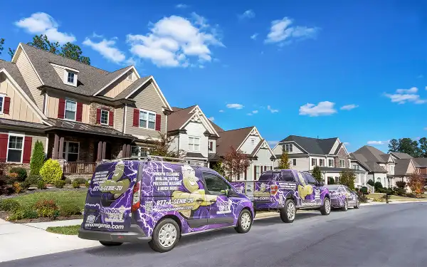 A residential street with three Window Genie vans parked on the side.
