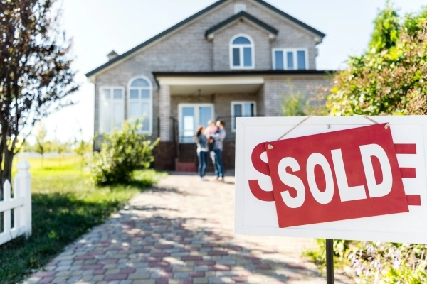 Sold sign in front of a home with young couple and baby blurred in the background.